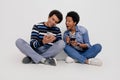 Surprised woman with mouth open looking at boyfriend's smart phone while sitting on white background Royalty Free Stock Photo