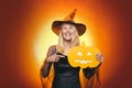 Surprised woman in witches hat and costume on red Halloween background. Attractive model girl in Halloween costume