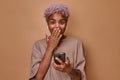 Surprised young African American woman holding mobile phone and covering mouth Royalty Free Stock Photo