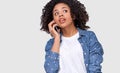 Surprised young African woman in white t-shirt and blue denim shirt, talking on smart phone to her friend, looking at one side, Royalty Free Stock Photo
