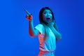 Surprised young Asian woman pointing to side and covers her mouth in surprise against blue gradient background in neon Royalty Free Stock Photo