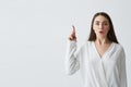 Surprised young beautiful businesswoman with opened mouth looking at camera pointing finger up over white background.