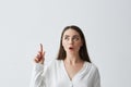 Surprised young beautiful businesswoman with opened mouth pointing finger up over white background.