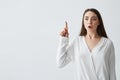 Surprised young beautiful businesswoman with opened mouth pointing finger up over white background.