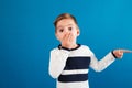 Surprised young boy in sweater pointing away and covering mouth Royalty Free Stock Photo