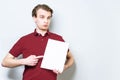 Surprised young business man in red polo shirt holding blank A4 signboard and pointing with finger at it. Business background with Royalty Free Stock Photo