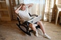 Surprised young caucasian man sitting on a rocking chair in a country house with a laptop,holding hands behind his head Royalty Free Stock Photo
