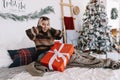 Surprised young caucasian woman with big Christmas present while sitting on a bed at home near Christmas tree Royalty Free Stock Photo