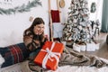 Surprised young caucasian woman with big Christmas present while sitting on a bed at home near Christmas tree Royalty Free Stock Photo