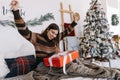 Surprised young caucasian woman with big Christmas present while sitting on a bed at home near Christmas tree Royalty Free Stock Photo