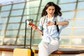 Surprised young european woman with suitcase with ticket and passport looks at watch, late for plane Royalty Free Stock Photo