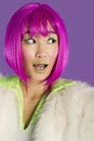 Surprised young funky woman in pink wig looking sideways over purple background