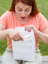 Surprised young ginger woman looking inside the paper bag in her hands. Female holding a white packet with food. Copy Royalty Free Stock Photo