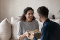 Surprised young hispanic woman taking wrapped box from young husband.