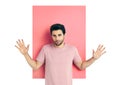 Surprised young man with arms up looking amazed in camera over pink and white background.