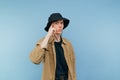 Surprised young man in casual clothes and panama stands on a blue background and shows his finger on his temple, looking shocked