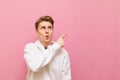 Surprised young man isolated on pink background and looks away and shows his finger on copy space. Guy in a white hoodie with Royalty Free Stock Photo