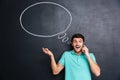 Surprised young man talking on mobile phone over blackboard background Royalty Free Stock Photo