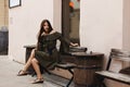 A surprised young woman with brown hair in a light summer dress sitting on the bench and looking aside.