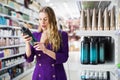 Surprised young woman choosing hair care products at cosmetics store Royalty Free Stock Photo