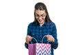 Surprised young woman in glasses and casual shirt looks in shopping bag, white background Royalty Free Stock Photo