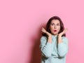 Surprised woman in light green hoodie looks at copy space. Horizontal studio shot on pink background