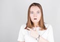 Surprised young woman points her finger to the space to her left. Portrait of a surprised girl on a gray background