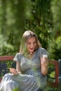 Surprised young woman reading text message on smart phone in park Royalty Free Stock Photo