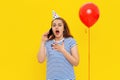 Surprised young woman is talking on a mobile phone, receives congratulations from friends on anniversary, wears party cone and Royalty Free Stock Photo