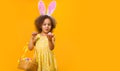 A surprized Black girl with rabbit ears on her head with a basket of colored eggs in her hands