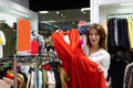 Surprized woman holding red dress in clothing shop and near is standing blank red tablet