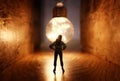 Surreal image of person in dark corridor looking at glowing light bulb. Concept of finding the right idea, or way out Royalty Free Stock Photo