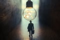 Surreal image of person in dark corridor looking at glowing light bulb. Concept of finding the right idea, or way out Royalty Free Stock Photo