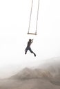 Surreal jump of a boy trying to hang himself in a swing that twirls in the sky, concept of risk and success Royalty Free Stock Photo