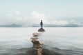 Surreal man reaches a rock in the middle of the lake through a stony road, concept of success