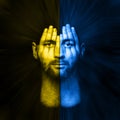 Surreal portrait of a man covering his face and eyes with his hands, face shines through hands, double exposure , flag of ukraine Royalty Free Stock Photo