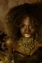 Surreal portrait of african american female model with glossy golden makeup posing to the camera on the studio
