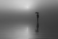 Surreal silhouette of a man in a suit and hat with an umbrella standing on the water