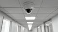 Surveillance camera mounted on a white ceiling in a modern hallway with bright overhead lighting and corridor doors in a secure Royalty Free Stock Photo