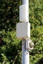 Surveillance equipment mounted on metal pole with security camera covered in protective glass next to wireless communication