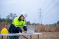 A surveying female electrical engineer wearing glasses is using a laptop computer and planning the construction of a high-voltage