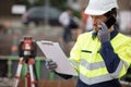 Surveyor with clipboard on site using smartphone