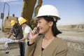 Surveyor in Hardhat In Front Of Workers Using Cellphone On Site