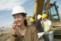 Surveyor in Hardhat In Front Of Workers Using Cellphone On Site