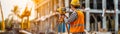 Surveyor using a theodolite at a construction site, wearing a hard hat and reflective vest. Building framework and cranes are