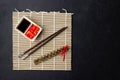 Sushi chopsticks, soy sauce, ginger, bamboo mat and empty plate on black background. Royalty Free Stock Photo