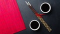 Sushi chopsticks, soy sauce, ginger, red bamboo mat and empty plate on black background. Royalty Free Stock Photo