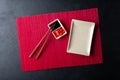 Sushi chopsticks, soy sauce, ginger, red bamboo mat and empty plate on black background. Royalty Free Stock Photo