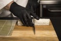 Chef cuts Japanese Sushi roll wrapped in rice with knife in protective gloves. Professional Cooking process in restaurant Royalty Free Stock Photo