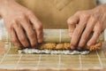 sushi preparation process, close up male hands rolls bamboo mat with sushi